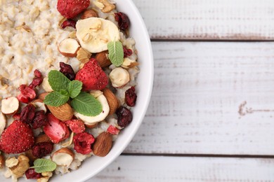 Photo of Delicious oatmeal with freeze dried berries, banana, nuts and mint on white wooden table, top view. Space for text