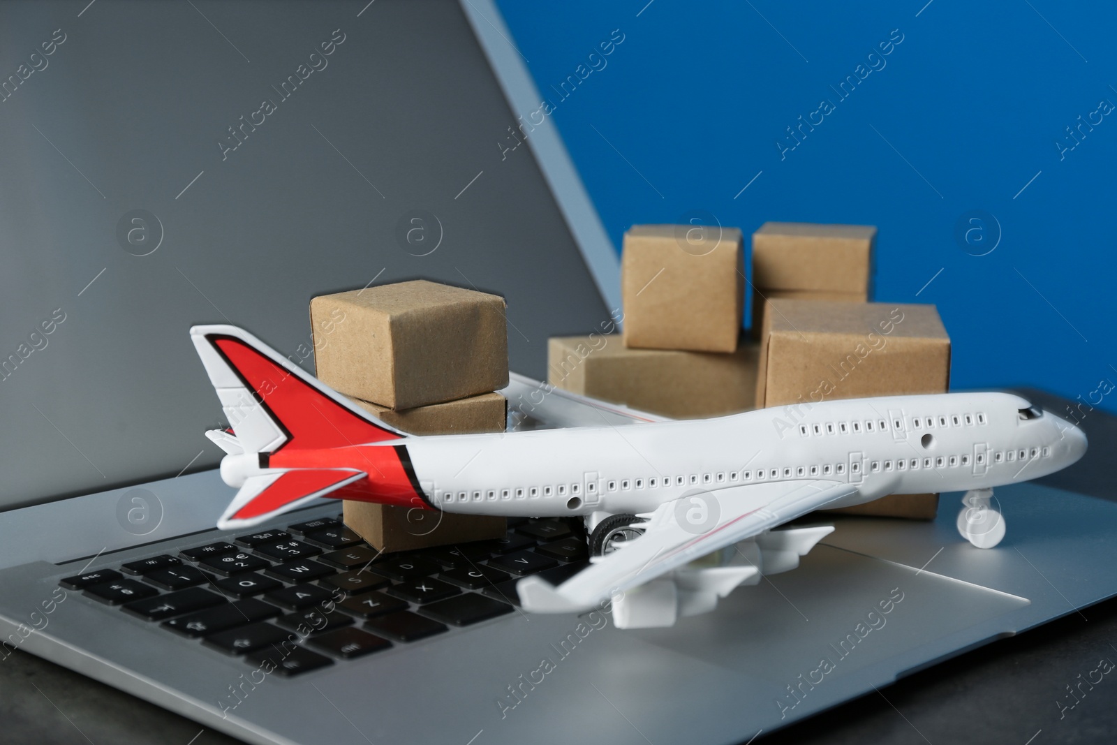 Photo of Laptop, airplane model and carton boxes on grey stone table, closeup. Courier service