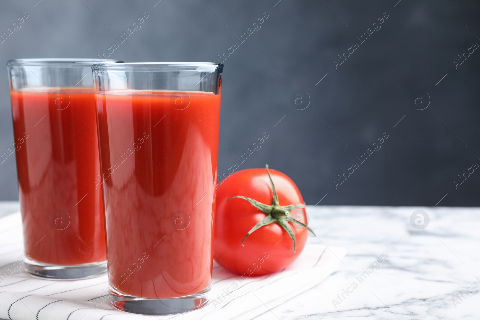 Photo of Delicious fresh tomato juice on white marble table, closeup. Space for text