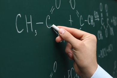 Photo of Teacher writing chemical formulas with chalk on green chalkboard, closeup