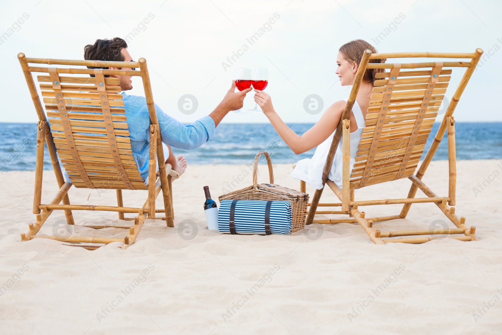 Photo of Happy young couple with glasses of wine sitting on deck chairs at sea beach