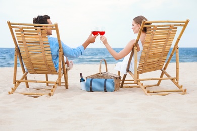 Happy young couple with glasses of wine sitting on deck chairs at sea beach