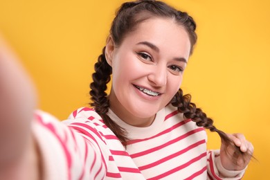 Smiling woman with braces taking selfie on orange background