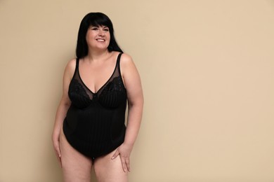 Photo of Beautiful overweight woman in black underwear on beige background, space for text. Plus-size model