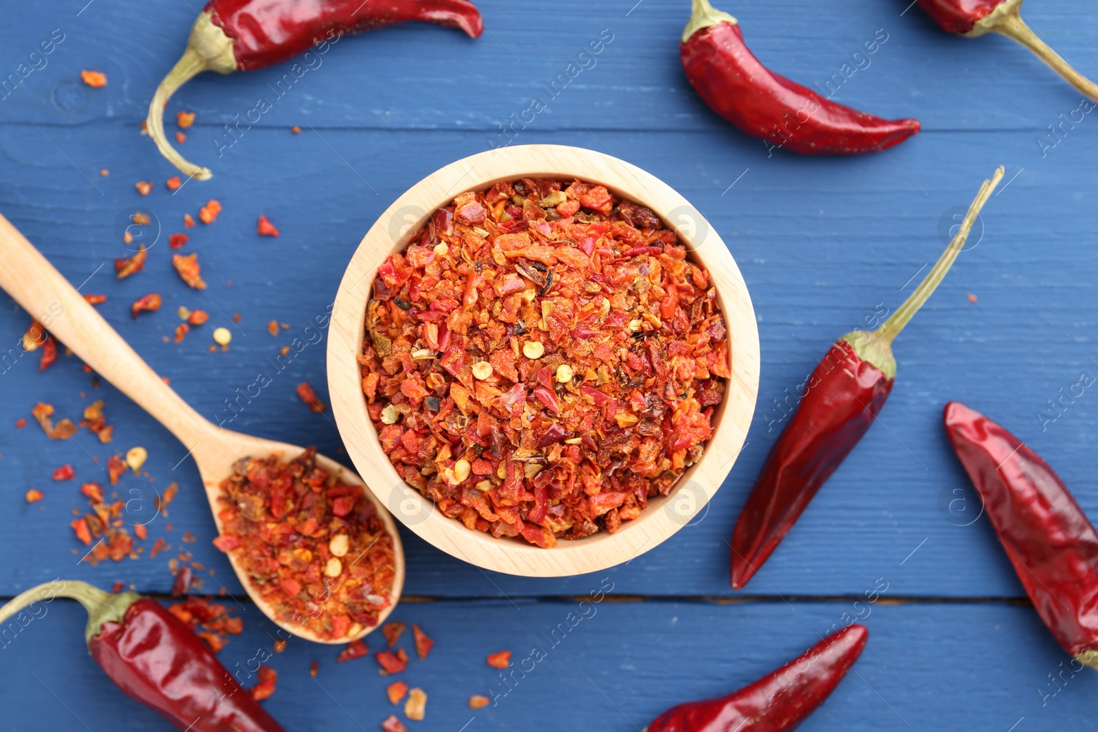 Photo of Chili pepper flakes and pods on blue wooden table, flat lay