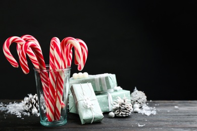 Photo of Many sweet candy canes, gift boxes and Christmas decor on black wooden table. Space for text