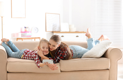 Photo of Happy mother and little daughter with mobile phone resting on sofa at home