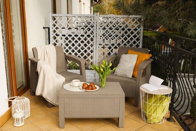 Photo of Different pillows, blanket, breakfast and tulips on rattan garden furniture outdoors