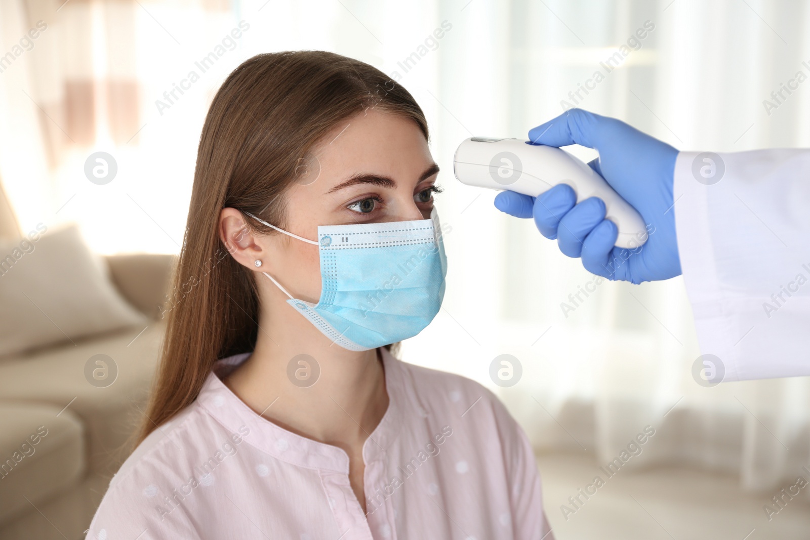 Photo of Doctor measuring patient's temperature with non contact infrared thermometer at home, closeup