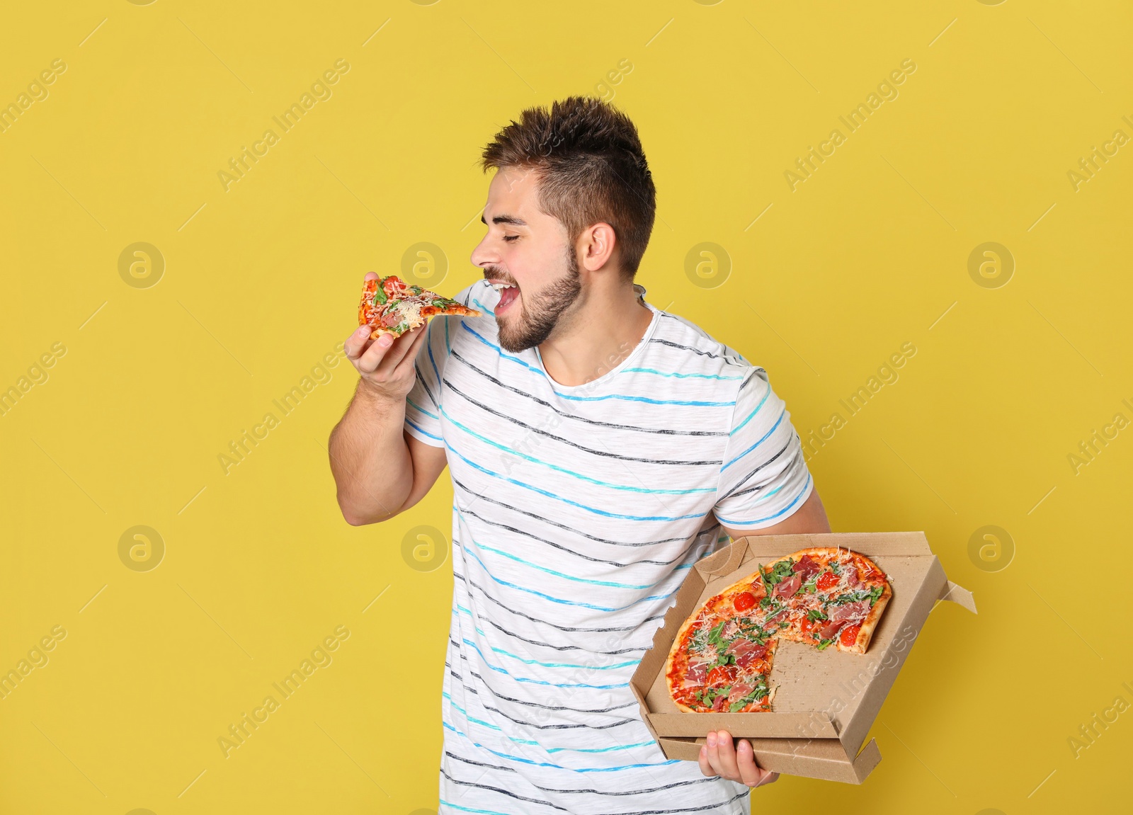 Photo of Handsome man eating tasty pizza on yellow background