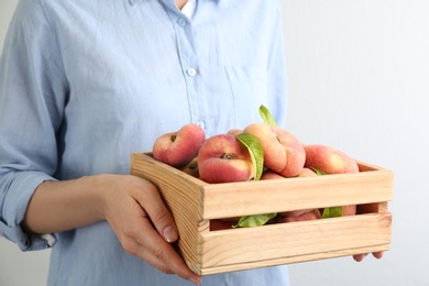 Photo of Woman holding wooden crate with fresh ripe donut peaches on light background, closeup