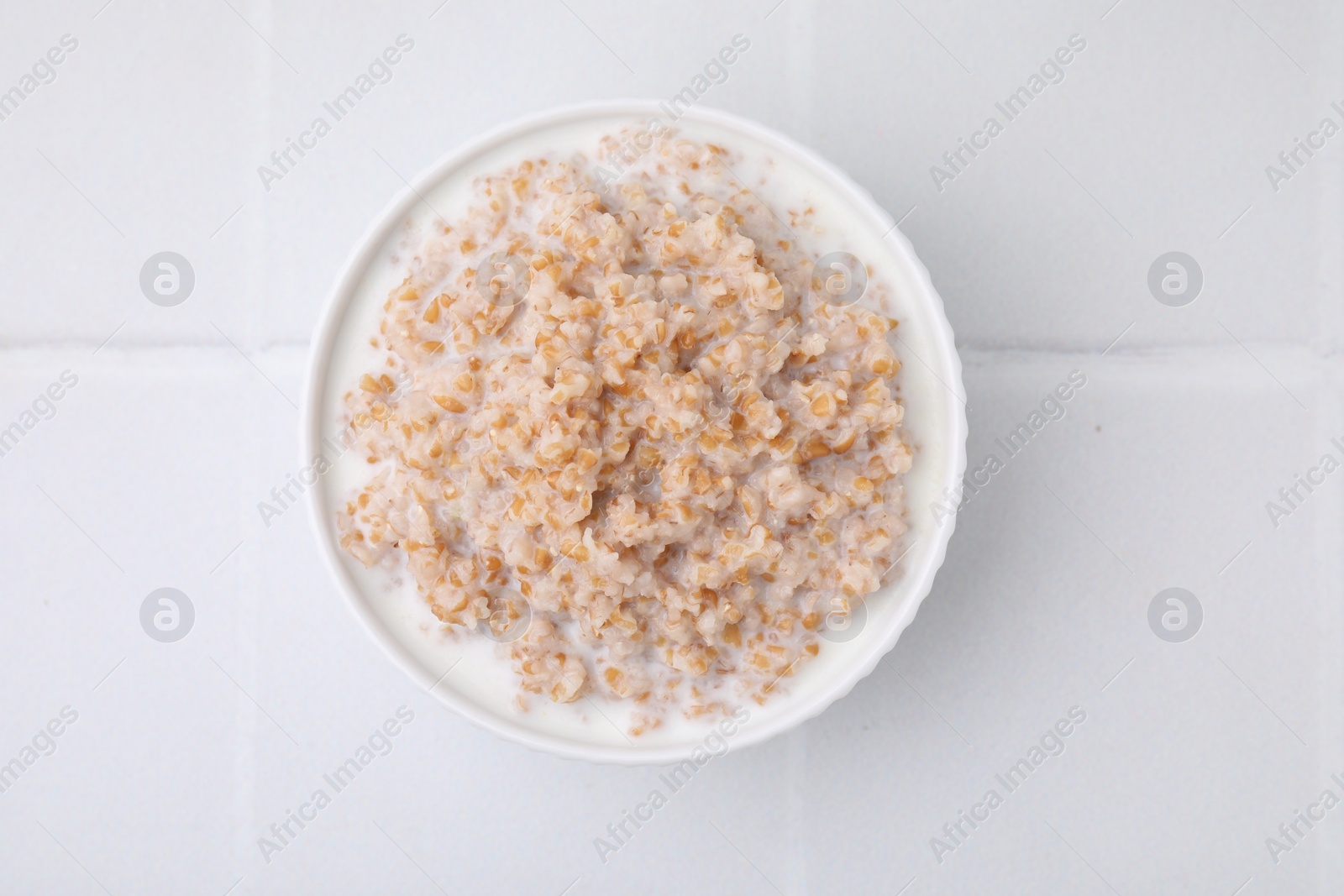 Tasty wheat porridge with milk in bowl on white table, top view Photo of Tasty wheat porridge with milk in bowl on white table, top view