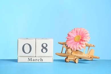 Photo of Composition with wooden plane and flower on table against color background, space for text. International Women's Day