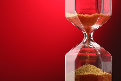 Photo of Hourglass with flowing sand on red background, closeup. Space for text