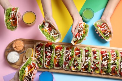Photo of Friends holding delicious tacos on color background, top view