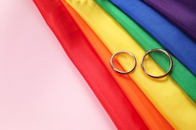 Photo of Rainbow LGBT flag and wedding rings on pink background, top view. Space for text