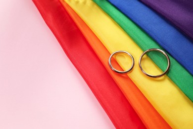 Rainbow LGBT flag and wedding rings on pink background, top view. Space for text