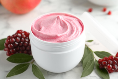 Photo of Fresh pomegranate and jar of facial mask on white marble table, closeup. Natural organic cosmetics