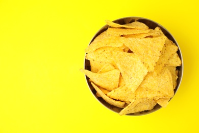 Photo of Bowl of tasty Mexican nachos chips and space for text on yellow background, top view. Space for text