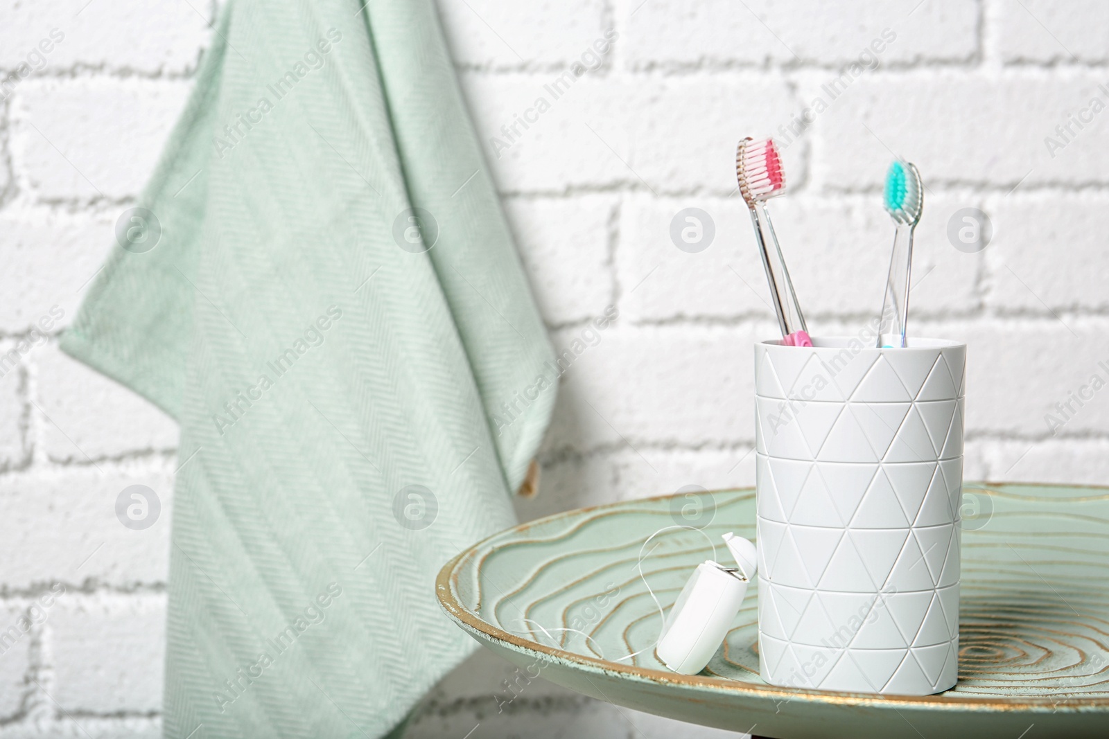 Photo of Cup with toothbrushes on plate against brick wall in bathroom