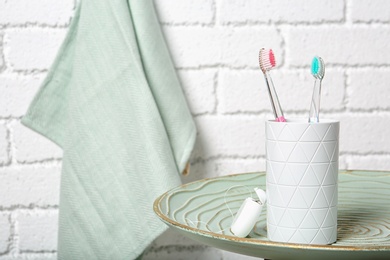 Photo of Cup with toothbrushes on plate against brick wall in bathroom