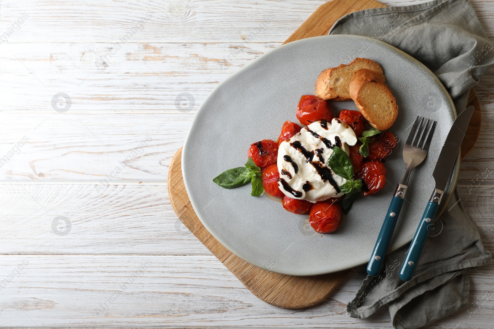 Photo of Delicious burrata cheese served with tomatoes, croutons and basil sauce on white wooden table, top view. Space for text