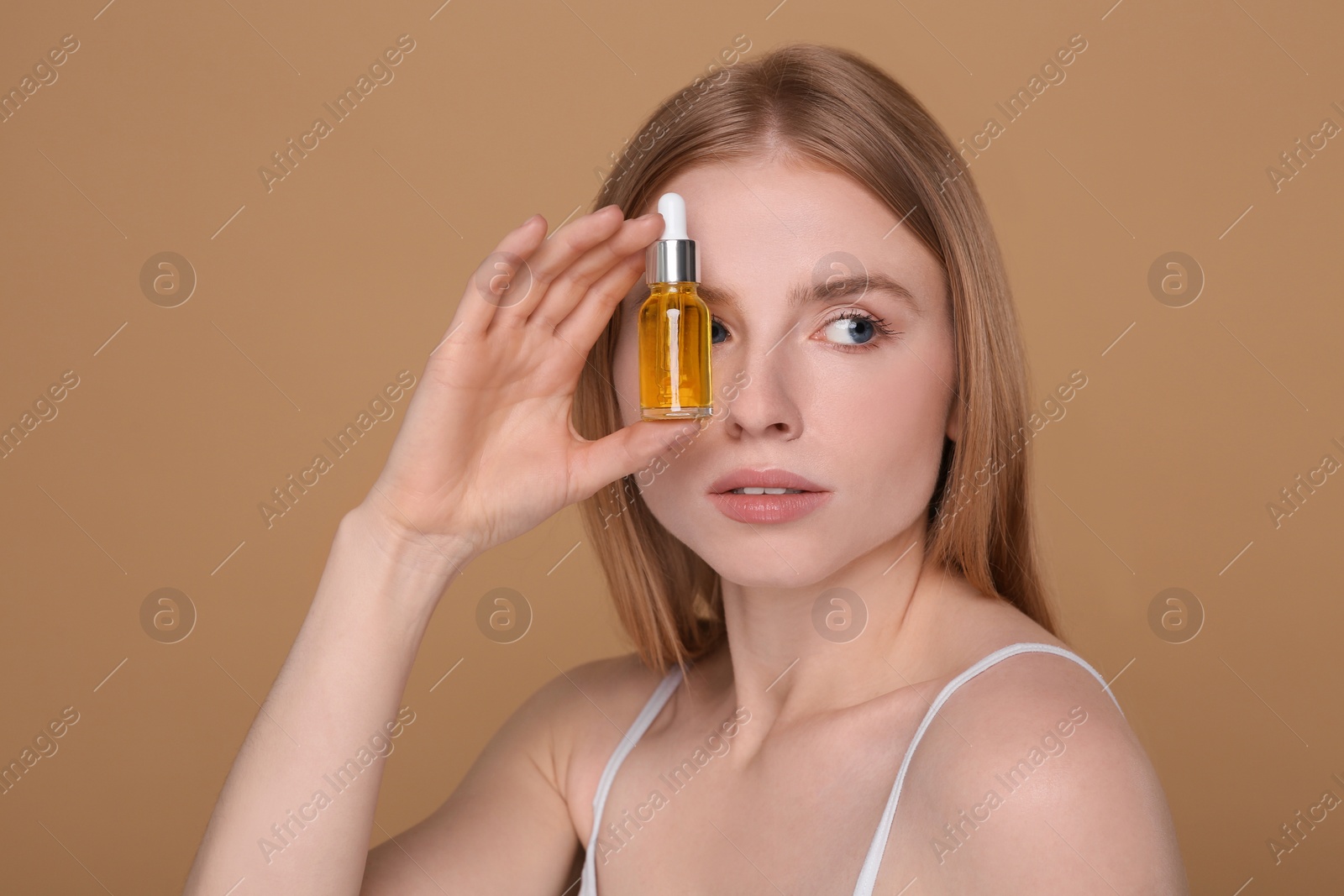 Photo of Beautiful young woman with bottle of essential oil on brown background