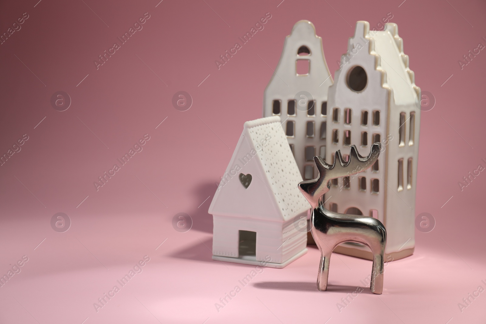 Photo of House shaped candle holders and silver deer on pink background, space for text