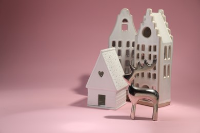 House shaped candle holders and silver deer on pink background, space for text