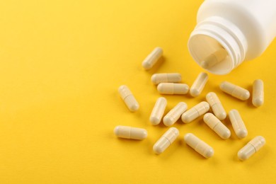 Photo of Bottle and vitamin capsules on yellow background, closeup. Space for text