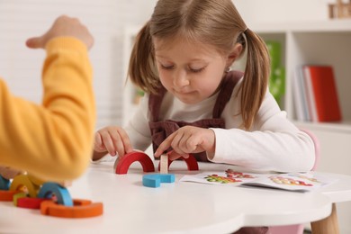 Photo of Little children playing with colorful wooden pieces at white table indoors. Developmental toy