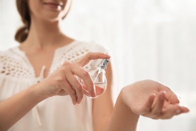 Photo of Young woman using perfume indoors, closeup