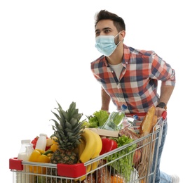 Young man in medical mask with shopping cart full of groceries on white background