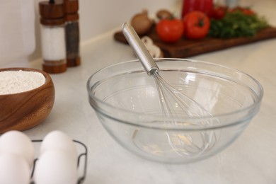 Metal whisk, bowl and different products on light table in kitchen