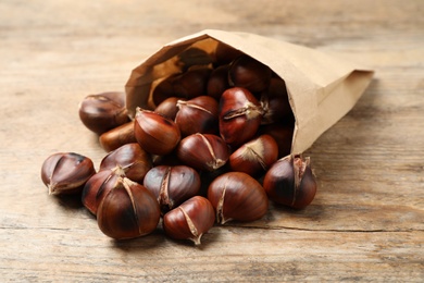 Delicious roasted edible chestnuts in paper bag on wooden table, closeup