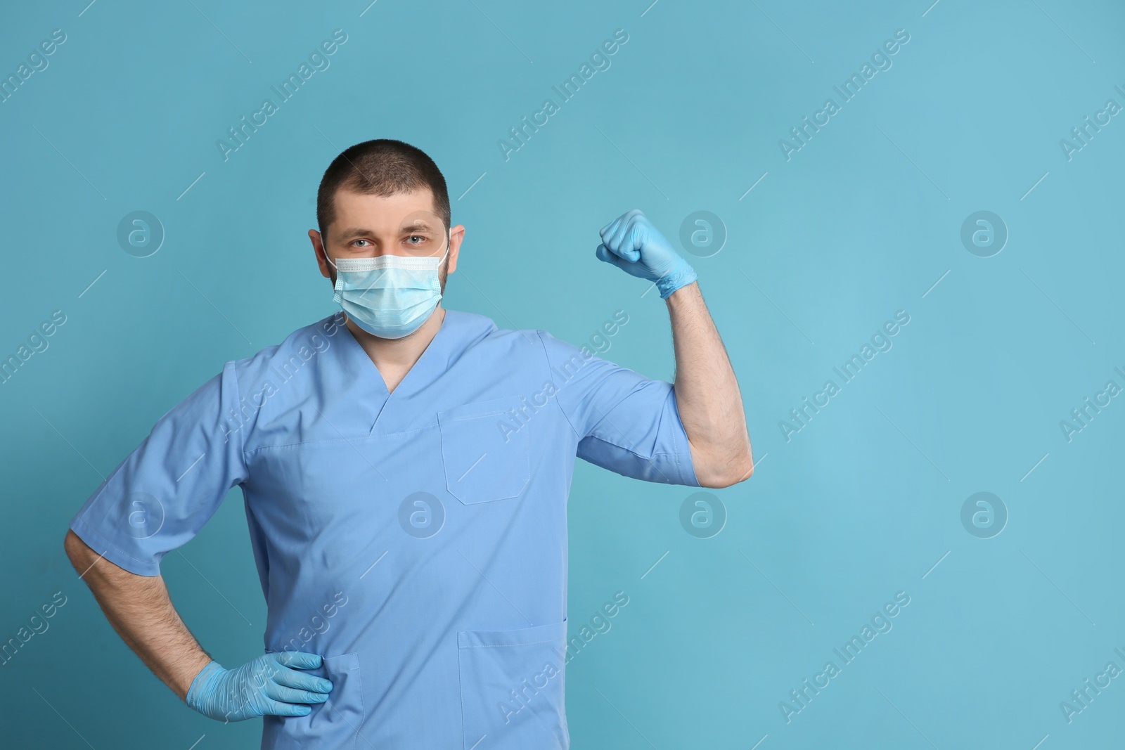 Photo of Doctor with protective mask showing muscles on light blue background, space for text. Strong immunity concept