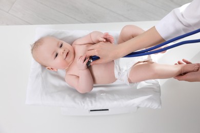 Photo of Pediatrician weighting and examining cute little baby with stethoscope in clinic, closeup