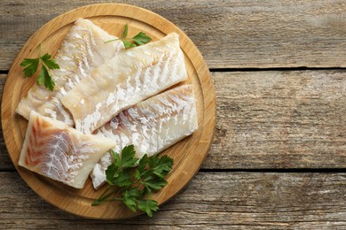 Photo of Fresh raw cod fillets and parsley on wooden table, top view. Space for text