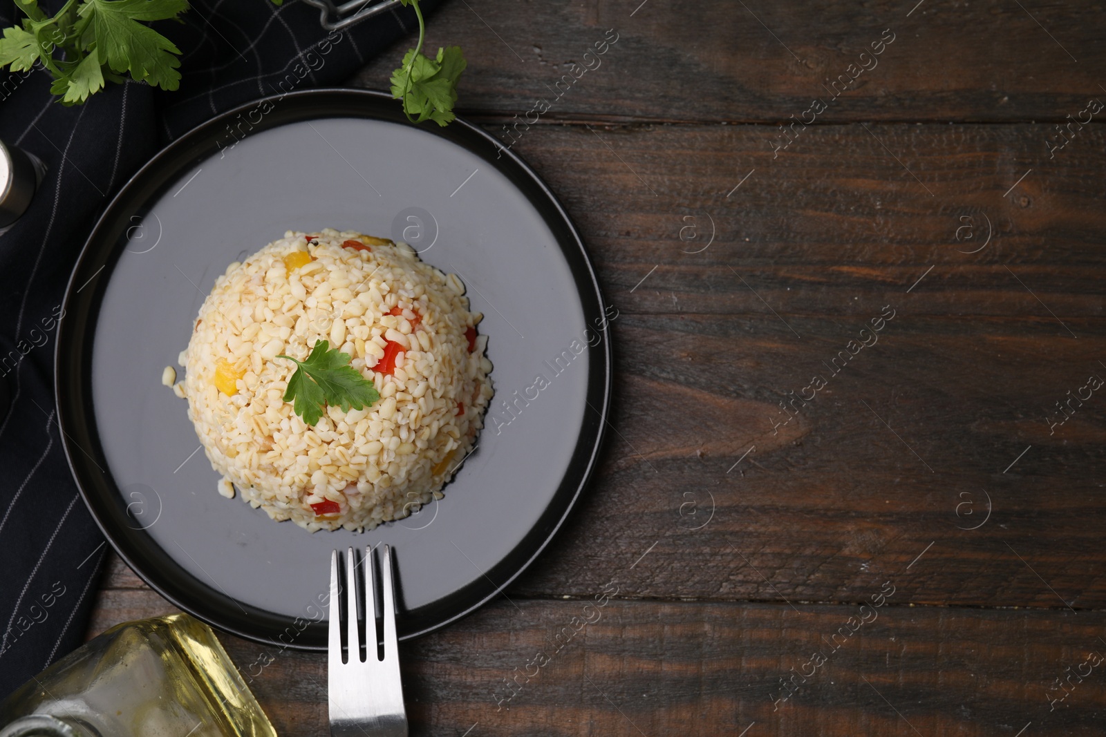 Photo of Delicious bulgur with vegetables served on wooden table, top view. Space for text