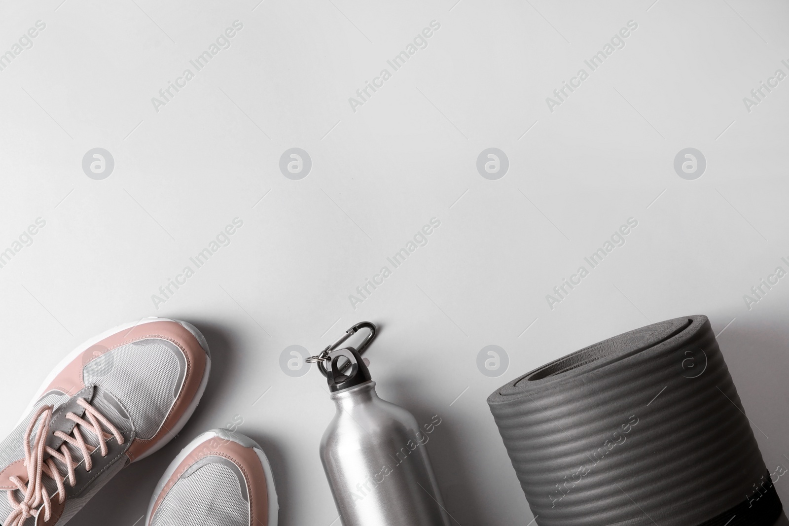 Photo of Yoga mat, sneakers and bottle of water on light background, top view with space for text. Fitness gym equipment