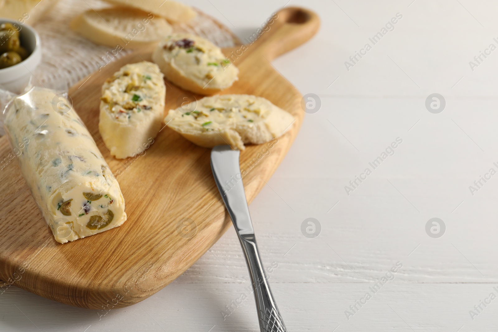 Photo of Tasty butter with olives, green onion, bread and knife on white wooden table, space for text