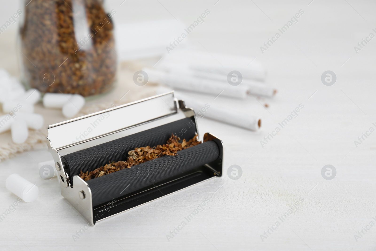 Photo of Roller with tobacco on white wooden table, space for text. Making hand rolled cigarettes