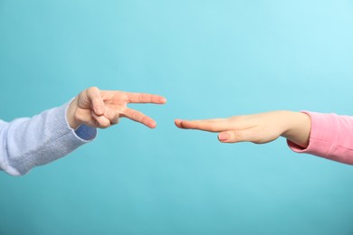 People playing rock, paper and scissors on light blue background, closeup