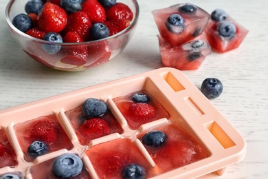 Photo of Ice cubes with berries in tray on table, closeup