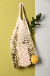 Photo of Conscious consumption. Net bag with eco friendly products hanging on color wall