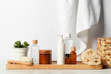 Photo of Different bath accessories and personal care products on light table near white wall