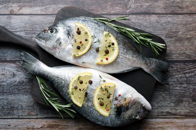 Fresh dorado fish, lemon slices and rosemary sprigs on wooden table, top view