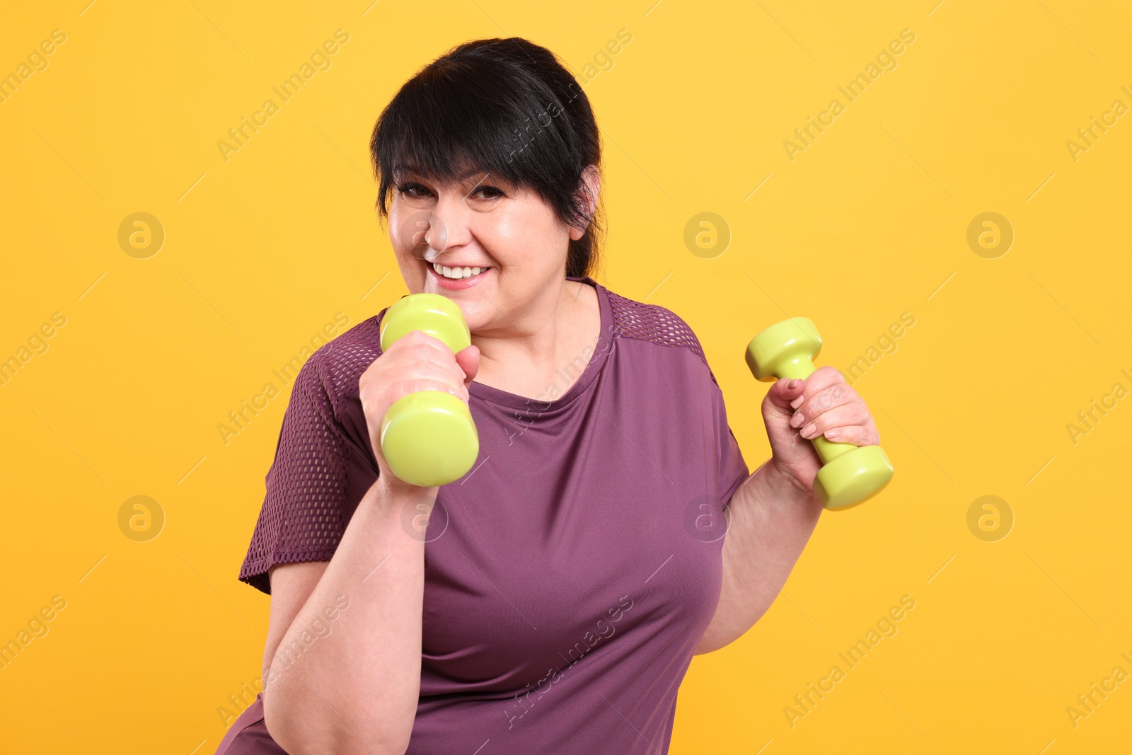 Photo of Happy overweight mature woman doing exercise with dumbbells on orange background