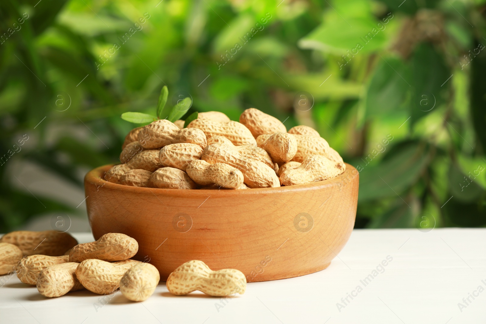 Photo of Fresh unpeeled peanuts in bowl on white table against blurred background