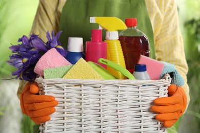 Woman holding basket with spring flowers and cleaning supplies outdoors, closeup